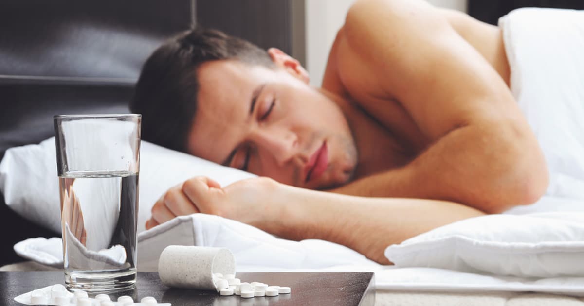 A man with sunburn sleeping on the bed with tablets and water on the side table