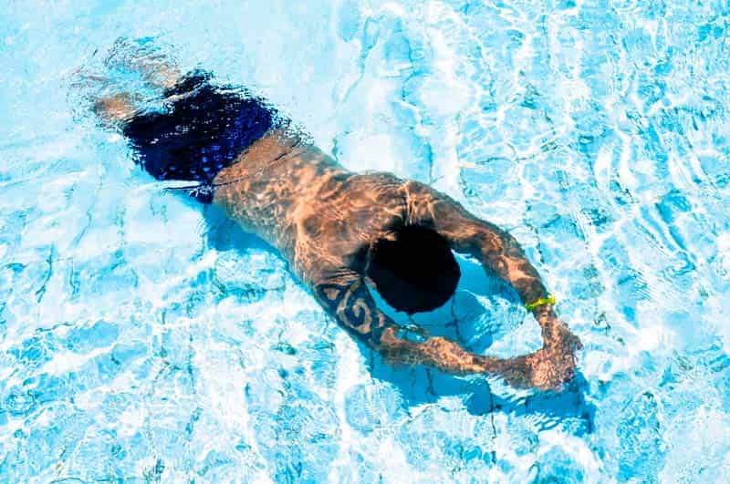 A man swimming under water, sunrays shining on his back